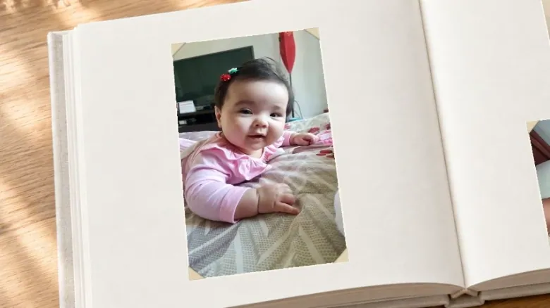 A photograph of a baby in a pink top in an open photo album on a wooden table.