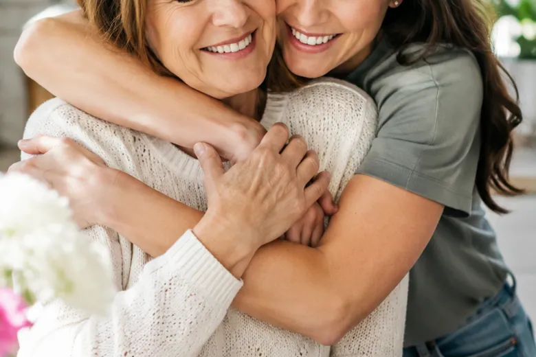 Two women embrace in a bright room.